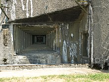 photographie en couleur d’un mur en béton percé d’une ouverture de tir