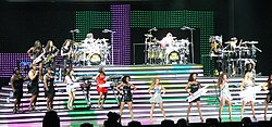 Several women performing a song on stage. Some of them are playing musical instruments, other are singing and dancing.