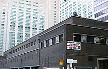 A dark modern brick building with lighter buildings rising to the top of the image behind it. On a corner in front is signage in French advertising offices for rent in the building