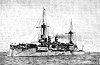 A large gray battleship with two tall masts sits motionless in the water