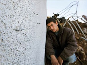 A Palestinian looks on as a small pointed metal dart known as a flechette, usually spread over a wide area in large numbers from a shell, is seen sticking out of the wall of a destroyed house in Mughraka, Gaza, on 21 January, 2009 (AP)