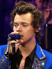A man with brown hair singing behind a microphone wearing an electric blue suit with sparkly lapels and cuffs