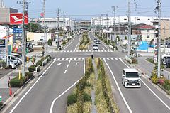 空港分岐線の分岐予定地（画像左）と愛知県道448号名古屋空港中央線（画像右）。25 mの広幅員道路の割に片側1車線となっているのは道路中央に名古屋高速の橋脚を建てるスペースを取っているためである（現在は片側2車線となっている。）[16]。7次空整への対応による知事の一元化発表以後、費用対効果の面で県の外部監査やマスコミに取りざたされ、事業の妥当性に疑問が付された[16][17]。