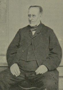 A black and white photograph of an older man, seated and wearing formal attire.