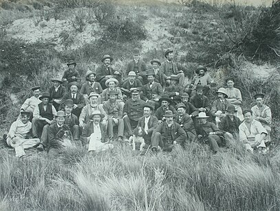 Photo of members of the Field Naturalists' Club of Victoria with Capt Anderson, some of the crew of Government steamer 'Lady Loch' & islanders and two dog, laying down on a sandy hillock. King Island, 1887