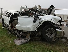 The severely damaged front left corner of a white stretch limousine