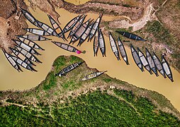 Bateaux ressemblant à des pirogues sur le lit d'une rivière accostés à un quai ou sur la berge. Il occupe pratiquement tout un coté de la rivière.