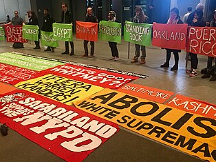 image of banners on floor of museum lobby, reading "Fuera Warren Kanders" and "Safariland Supports the NYPD"