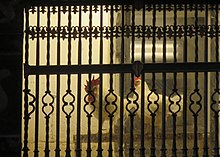 A cock and a hen behind wrought bars.