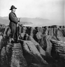 A soldier in uniform with a rifle looking out to see standing atop the Pancake Rocks at Punakaiki