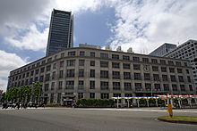 Ground-level view of a stone, low-rise building; two window-dotted facades are connected via a curved corner