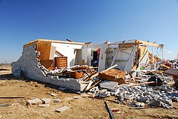 The remains of a home, now mostly a pile of rubble; part of the structure remains intact.