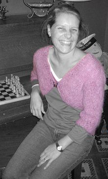An woman wearing a pink wool knit shrug. The image is in greyscale aside from the shrug.