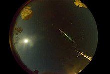 Fish-eye-lens photograph capturing streaking fireball in the night sky