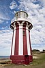 Hornby Lighthouse, a tapered circular structure painted with red and white vertical stripes, with a white balcony and railing, and glass lantern