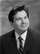 Portrait en noir et blanc d'un homme aux cheveux bruns courts au visage plutôt rond, souriant.