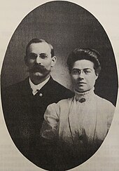 Black and white oval-shaped photo of a middle-aged man and woman sitting beside each other in formal clothing
