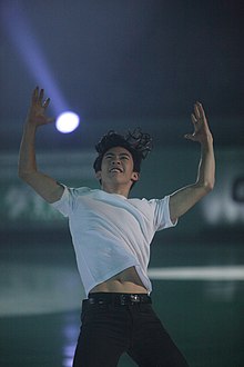 A photograph of Nathan Chen smiling during an exhibition performance under colourful lights.