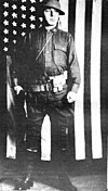 Oscar Pfaus in uniform, standing in front of a U.S. flag