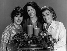 Three women standing around a candle in a black-and-white photo