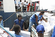 A couple of Liberian citizens (wearing blue vests that read World Food Program) unload weights of food to other citizens.