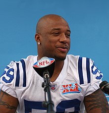 African American male in football uniform seated at a press conference with an NFL logo on the microphone