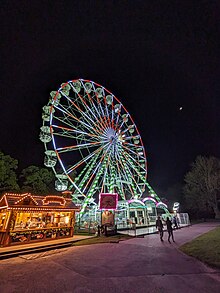 Observation wheel illuminated by multicoloured lights at spotlights at nighttime against a pitch black sky.