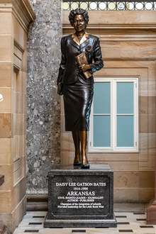 Bates wears a dark suit with a button detail on the pockets and a lighter blouse with the collar layered over the suit lapels. Her impeccable appearance indicates both her personal style and her role as a leader in Little Rock's business community. She and her husband, L.C., published the Arkansas State Press, which focused on the African American community and consistently pressed for civil rights.