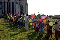 Groupe d'enfants portant des ballons de baudruche et en arrière desquels le chevet d'une église abbatiale est visible.