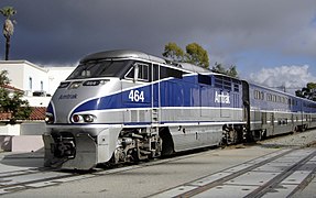 A passenger train with bilevel passenger cars painted in gray and blue stripes. The blue stripe on each side tapers to a point on the nose of the locomotive.