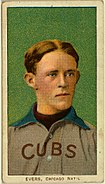 A man with blonde hair wearing a grey baseball uniform with a blue collar and the word "CUBS" on his chest in front of a green background