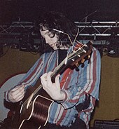 A man performing live onstage with an acoustic guitar.