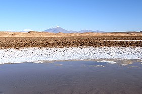 Photo of land rising above a lake, with a white capped mountain