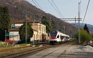 White and red train next to a two-story stuccoed building with gabled roof