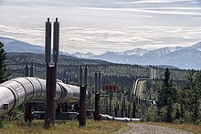 A large black pipe supported by rust-covered goal posts snakes through Alaskan hills and mountains into the distance