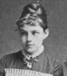 A young woman with hair in an updo with short curled bangs, wearing a high-collared dress with a striped pinafore apron