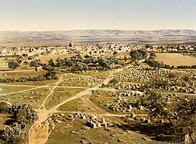 A colorized skyline of a town with hills on the horizon, white buildings in the background, and a cemetery, olive trees, and dirt paths in the foreground