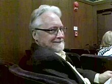 Photograph of a white man in his late 60s with glasses and a beard.