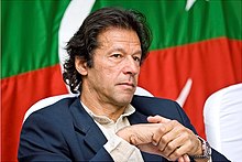 Imran Khan, seated in front of a Pakistani flag