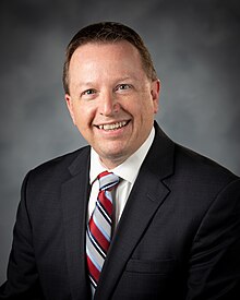 A man in a suit smiling at the camera, with a grey background