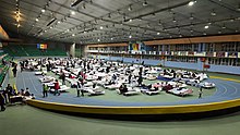 An indoor sports hall with people on camp beds inside a running track