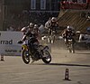 Supermoto motorcycles transition from dirt obstacles to paved track.