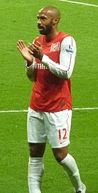 Thierry Henry, wearing a red shirt with white long sleeves and shorts with a number 12 and Nike logo on the left-leg side, applauds.