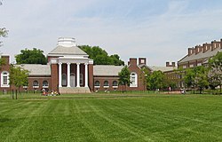 A brick neoclassical building topped by a dome and fronted by four white columns, with a green lawn in the foreground