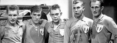 A black and white photograph of five football players standing beside each other in a locker room after a match. The players are noticeably tired; large sweat stains are visible on their shirts.