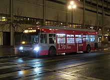 A silver bus on a wide street at night