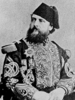 Mott as an Egyptian military officer, a middle-aged man with a full beard wearing an elaborate uniform with a fez