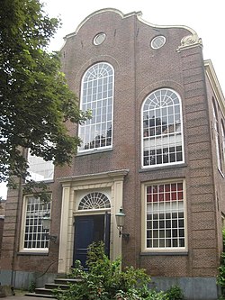 High angle of a facebricked facade of a synagogue with entrance and five windows. Sky and trees also feature in the image.