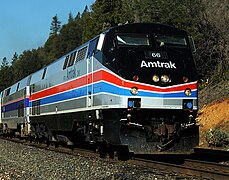 A gray diesel locomotive with a black cab area. Red and blue stripes separated by thin white stripes run along the sides and wrap across the front, where they pinch slightly