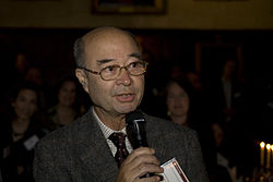 Mechai Viravaidya wearing a suit and tie, speaking into a microphone, looking left of camera